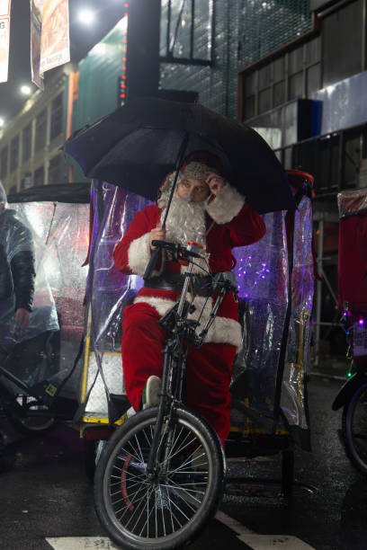 A pedicab operator dressed as Santa and Holding an Umbrella on a rainy night in Manhattan New York city