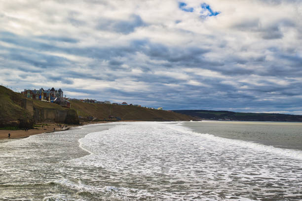 istock Coastal Scene with Beach, Town on Cliffs, and Cloudy Sky in Whitby, UK. 2204470259