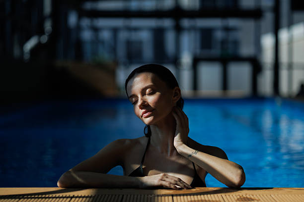 Relaxed woman standing in sunlight at poolside in spa complex