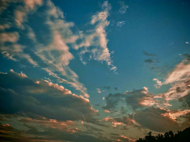Sky panorama with soft clouds tinged pink and orange during sunset. Blue sky and fluffy clouds create a serene and beautiful scene.
