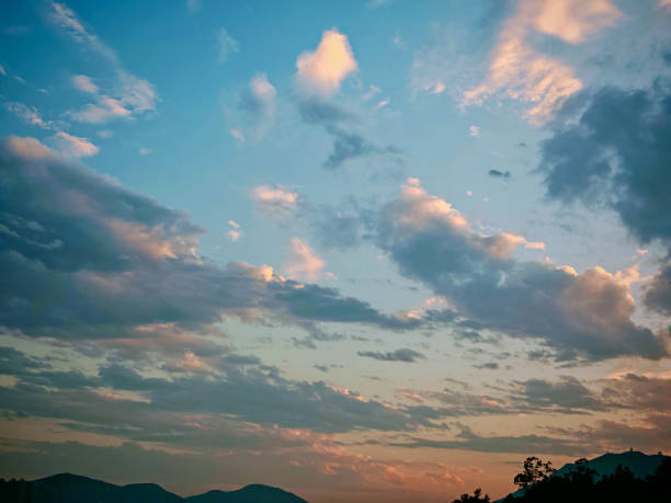 A serene sky at dusk is filled with soft, illuminated clouds. The horizon shows a hint of mountains, suggesting a peaceful, natural scene.
