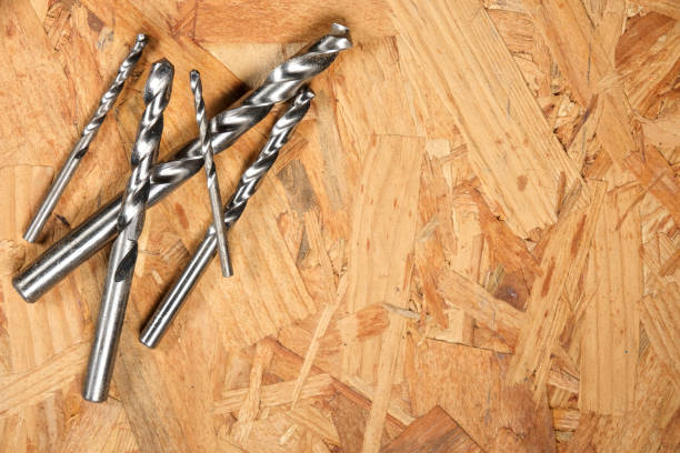 istock A set of metallic drill bits of various sizes rests on a textured oriented strand board (OSB) surface, showcasing their sharp edges and reflective surfaces. 2204481100