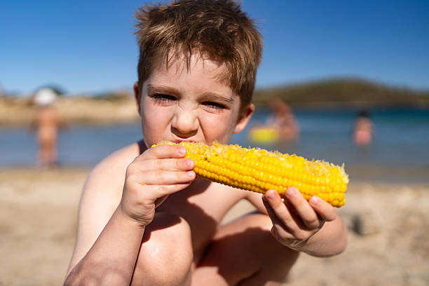 Little boy eating sweetcorn on the beach.
