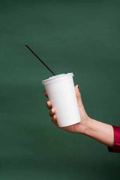 A simple yet stylish image featuring a hand holding a white disposable takeaway cup with a black straw, set against a deep green background. The minimalistic composition highlights the concept of takeaway beverages, whether it be iced coffee, milk tea, smoothies, or other cold drinks. This clean and modern aesthetic makes it a perfect visual for branding, cafe promotions, or advertising refreshing beverages on the go.