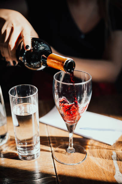 istock Red wine being poured into a glass on a rustic wooden table with warm natural lighting, Elegant dining and wine appreciation moment, Fine dining experience in a cozy restaurant setting 2204489635