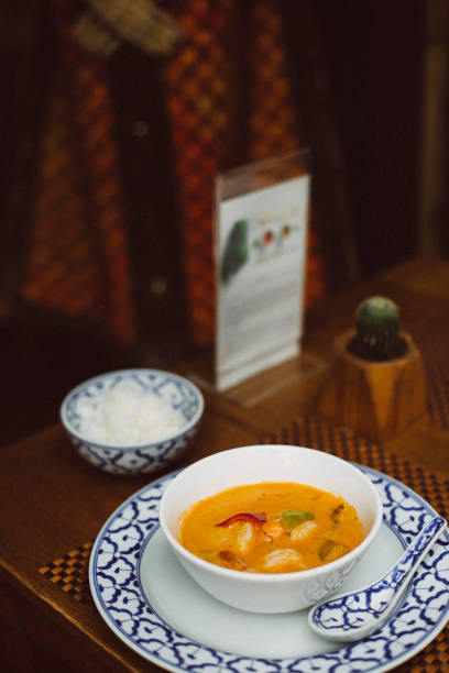 istock Traditional Thai tom yum soup with shrimp served in a ceramic bowl with blue patterns, accompanied by steamed jasmine rice on a rustic wooden table in an authentic restaurant setting 2204490309