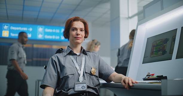 istock Portrait of Female Security Officer Looking at Camera. Computer Screens Showing X-ray Baggage Scanning 2204491467