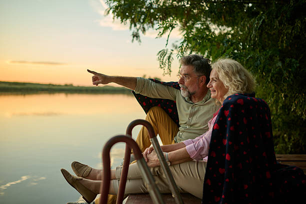 istock Senior couple enjoying sunset over lake while sitting on pier 2204491577