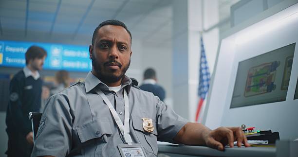 istock Portrait of TSA Worker Looking at Camera. Computer Screens Showing X-ray Images 2204491788