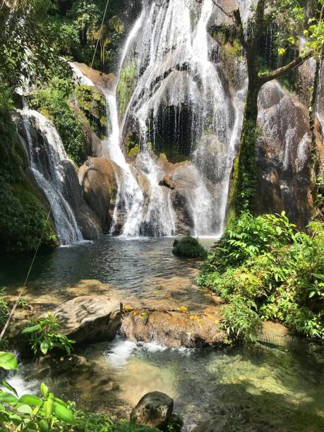 istock Serene waterfall cascading over rocks surrounded by lush green foliage on a sunny day 2204491954