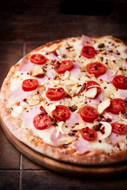 istock Pizza with ham, cherry tomatoes and mozzarella cheese. Wooden background. Soft focus. Close up. 2204492505
