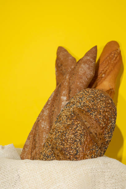 Vertical image of whole grain breads in a basket with rustic white cloth on a yellow background. Nutritious food with high fiber content