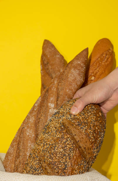 istock Vertical image of a male hand taking a whole wheat bread that is inside a basket full of whole wheat breads on a yellow background 2204494081