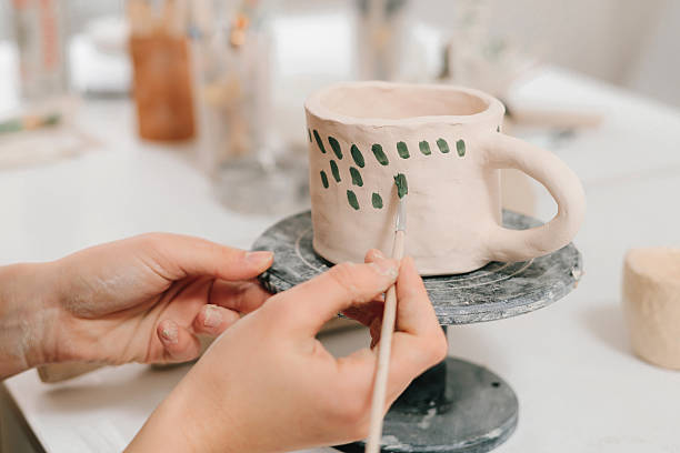 istock Artist is decorating and painting handmade ceramic clay cup in the creative workshop. Painter is drawing and adding unique designs to the earthenware. 2204495552