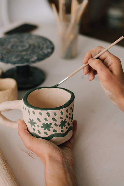 istock Potter draws an abstract design into earthenware cup. Experienced artist painting designs on ceramic cup in pottery workshop. 2204495762