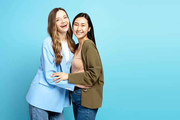 istock Two happy smiling young women embracing on blue background 2204495763