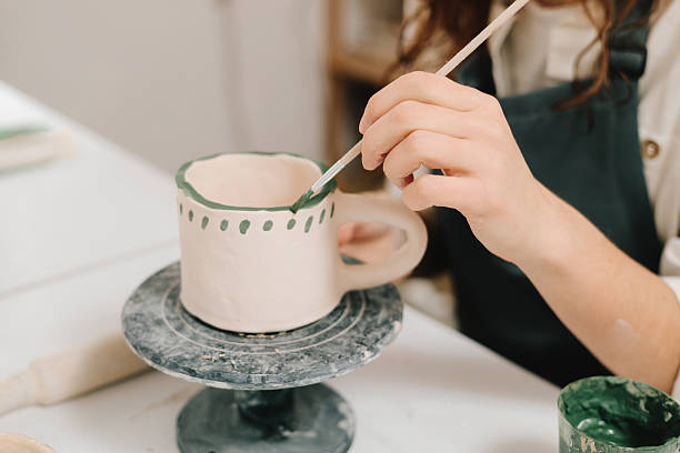 istock Artist is decorating and painting handmade ceramic clay cup in the creative workshop. Painter is drawing and adding unique designs to the earthenware. 2204495878