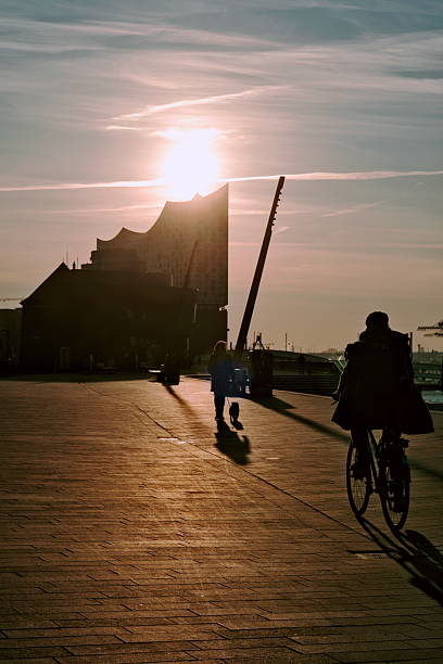 The sun rises behind the Elbphilharmonie, with silhouettes of pedestrians in the foreground against the backlight.