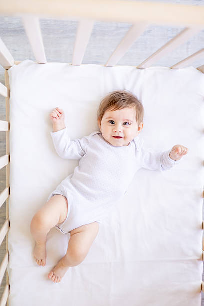 istock a small child close-up on a white cotton bed at home is lying on a split in a white bodysuit and smiling, a baby girl with big eyes of six months, top view 2204498681