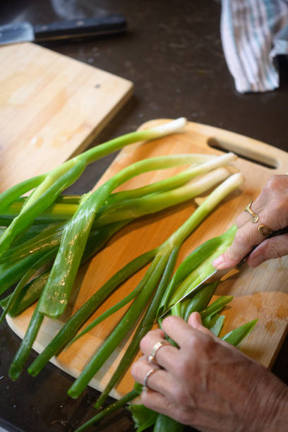 istock Hands Chopping Fresh Green Onions on a Wooden Cutting Board in Kitchen 2204501650