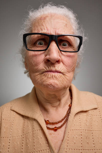 Grumpy old woman looking nervous, skeptical and displeased on a gray background