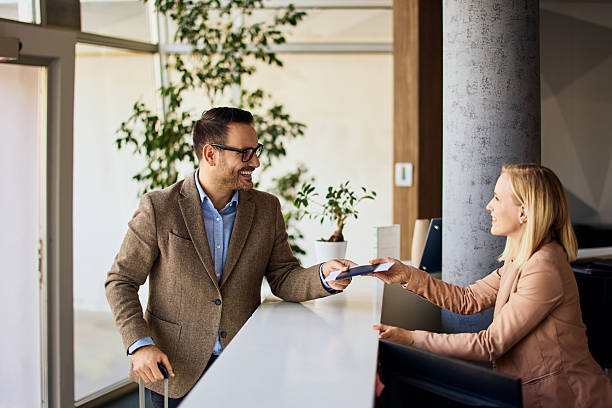 Smiling Man Checking In with Receptionist at Office Desk stock photo