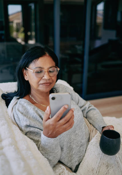 istock African woman sitting on sofa drinking coffee while using mobile phone 2204512406