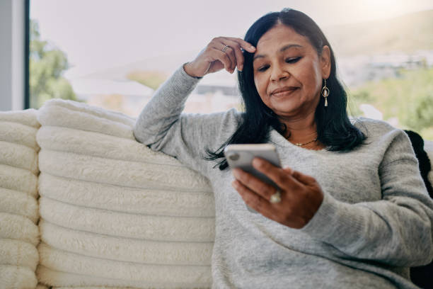 istock Mature woman text messaging using mobile phone at home 2204512443