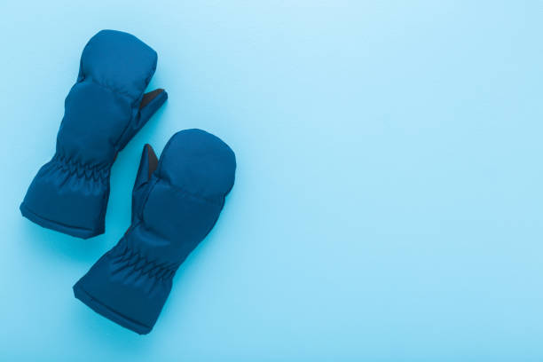 Pair of dark blue waterproof warm winter mittens for kid on light blue table background. Pastel color. Closeup. Empty place for text. Top down view.