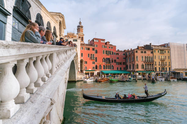 Venice, Italy - 12 October 2024: a gondola passes under the Rialto bridge as tourists watch from above