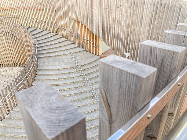istock A weathered spiral staircase with alternating light and dark steps, supported by wooden posts, in an indoor modern setting A person is seen using the handrailed staircase 2204516672