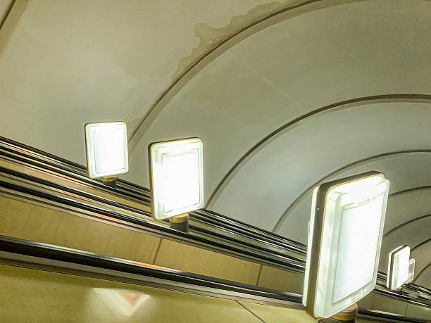 istock Image shows an interior view of a subway or underground transport system with a metallic escalator, three light fixtures on the ceiling, and a reflective surface The color palette is neutral 2204516736