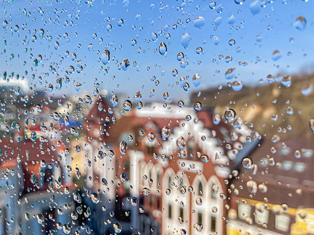 istock A rainy urban scene with residential buildings, trees, and soft, diffused sunlight through raindrops on a window Warmth and homeliness conveyed by muted yet vibrant colors Birds eye view, with foc 2204516747