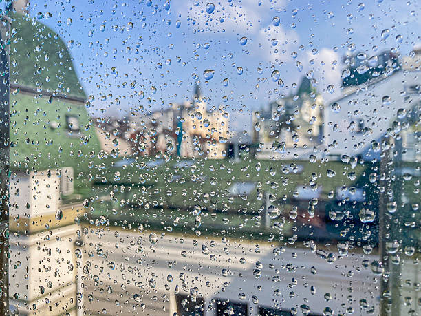 istock Image depicts an urban setting, post-rain scene through a window Droplets on glass reflect buildings and blue sky with clouds 2204516780
