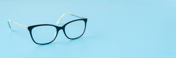 istock Eyeglasses with dark black plastic frame on light blue table background. Pastel color. Wide banner. Closeup. Empty place for text. Front view. 2204516871