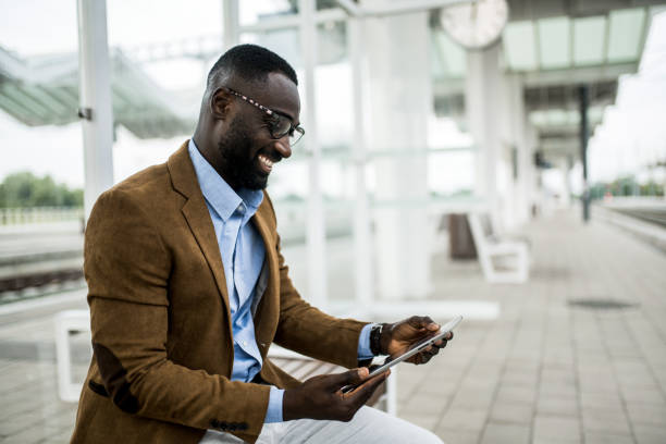 istock Happy black businessman working on digital tablet while waiting for train on railway station. 2204517393