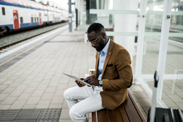 istock Black businessman working on digital tablet while waiting for train on railway station. 2204518674