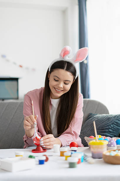 istock Young woman painting easter eggs at home wearing bunny ears 2204520907