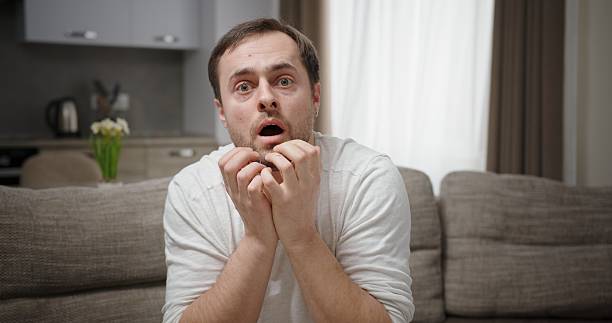 istock An anxious man is watching television with an intense focus that displays many emotions 2204521345