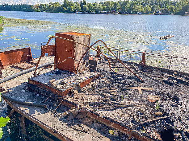 istock Image depicts a dilapidated dockpier partially submerged in water with greenish algae Surroundings contain debris and a discarded metal container Background shows trees along a shoreline, suggesti 2204522147