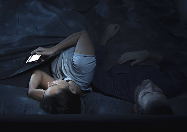 istock Woman chatting with her smartphone at night while her husband is sleeping 2204525104