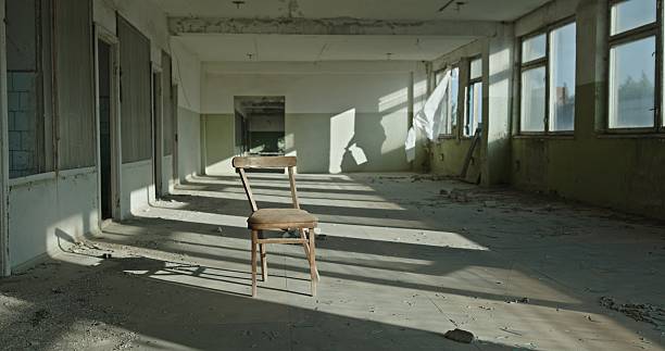 Natural light from a broken window illuminates a single chair in an abandoned government building.