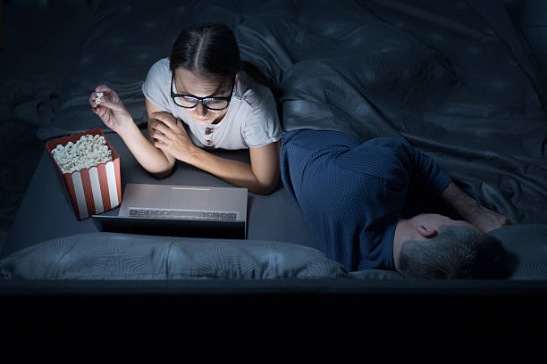 istock Woman watching movies online while her husband is sleeping 2204525898