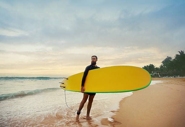 Young  bearded man with surfboard standing near a beach. Man with surfing board outdoors on a summer day