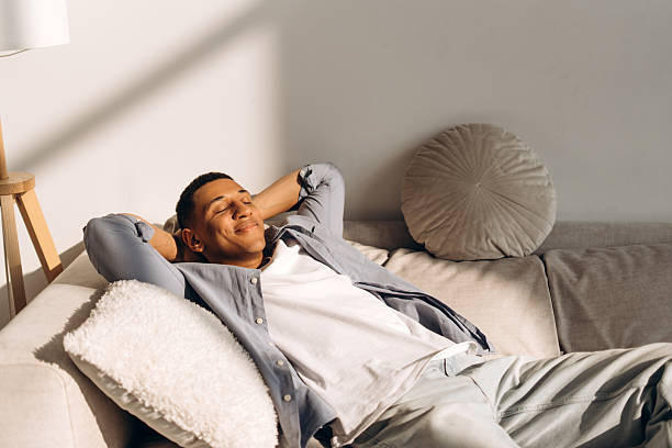 istock Young man relaxing on sofa enjoying sunlight in living room 2204536668
