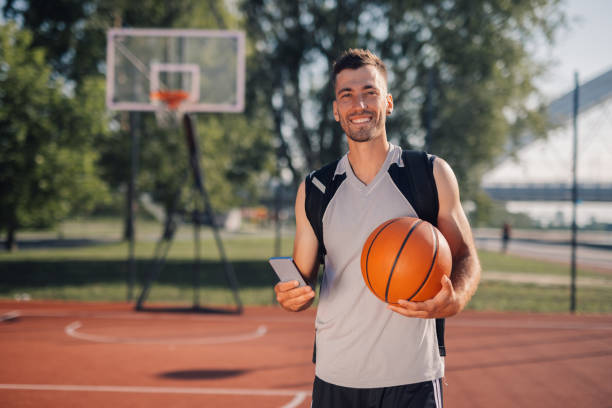 istock Smiling basketball player holding ball and using smartphone on court 2204537079