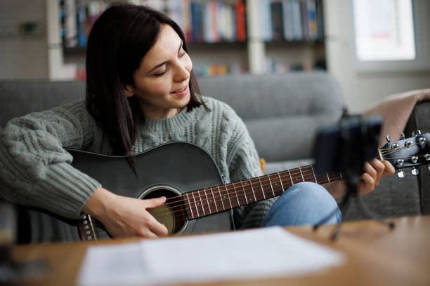 istock Smiling young woman learning to play guitar while watching lessons on her smartphone at home 2204544278