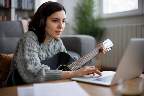 istock Woman learning to play guitar online, following her virtual lesson 2204544351