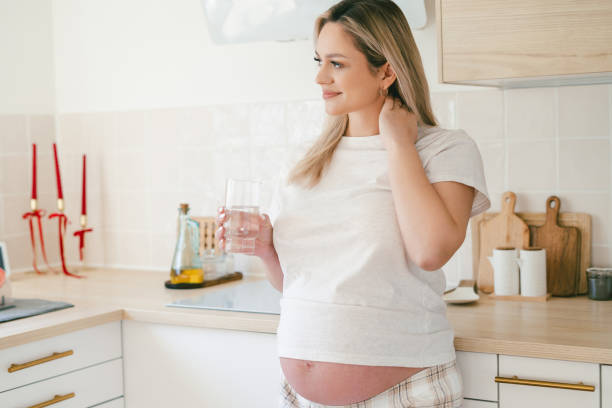 istock Young beautiful pregnant woman drinking water at home in the kitchen. 2204546708