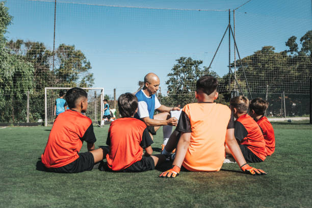 istock coach sitting with boy soccer team on pitch and drawing on match board 2204547098